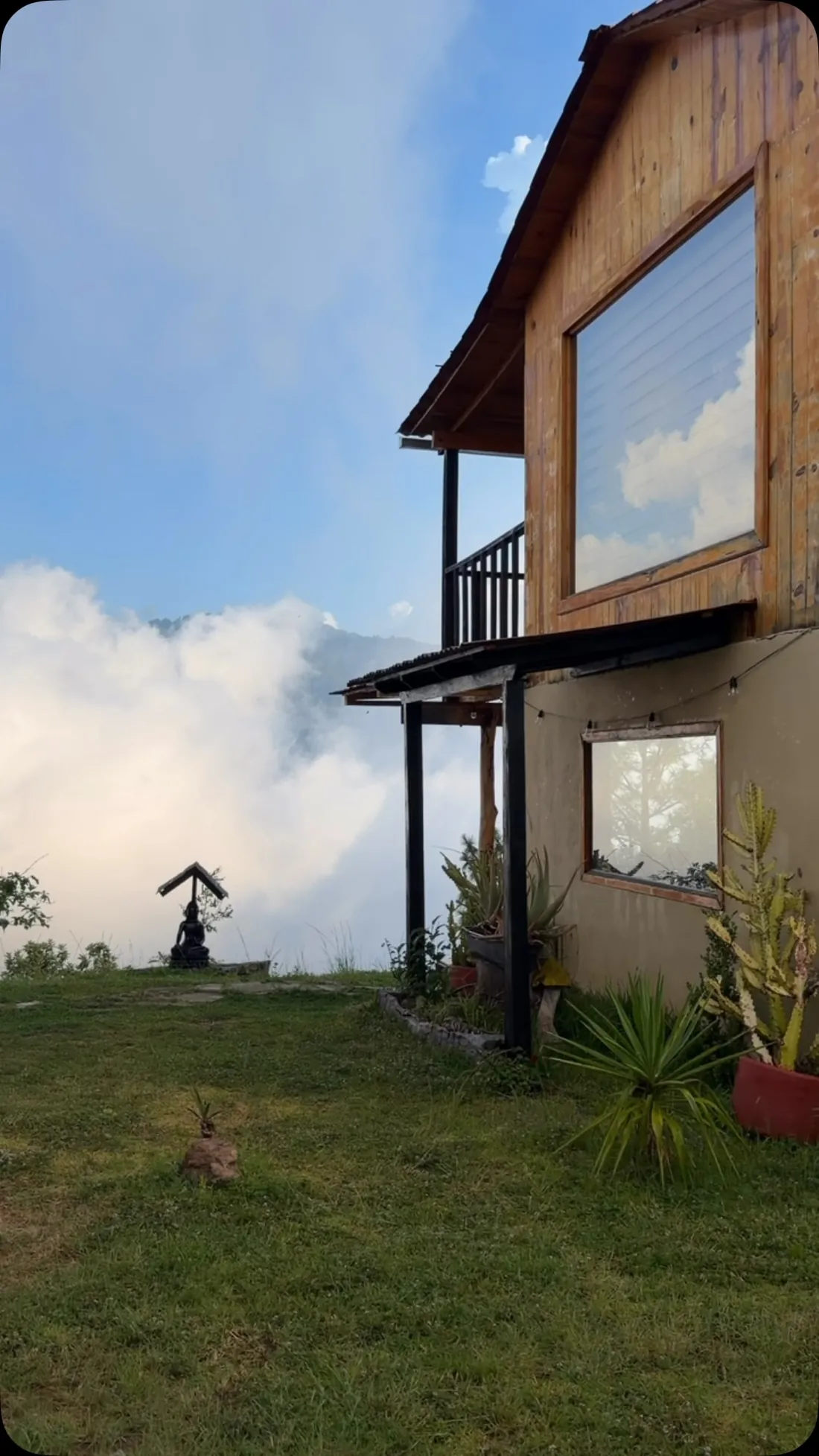 Cabaña Nube: casa de madera de dos pisos con balcón, junto al pasto y las nubes.