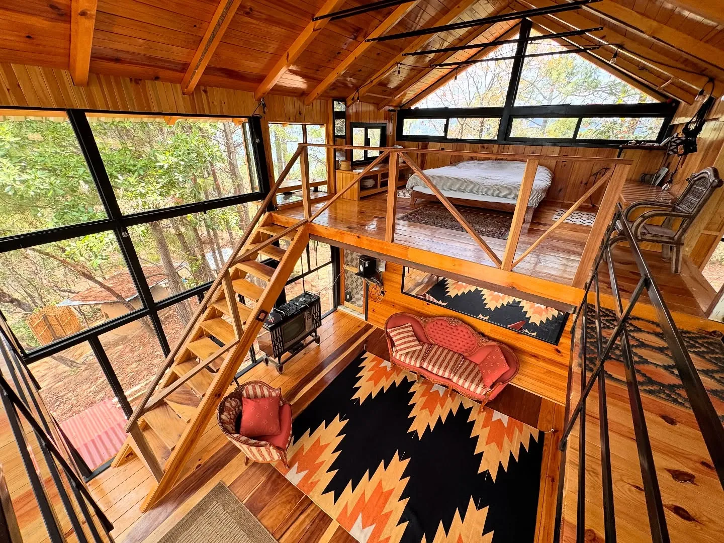 Doble altura de Casa Tierra con escalera de madera y tapetes.