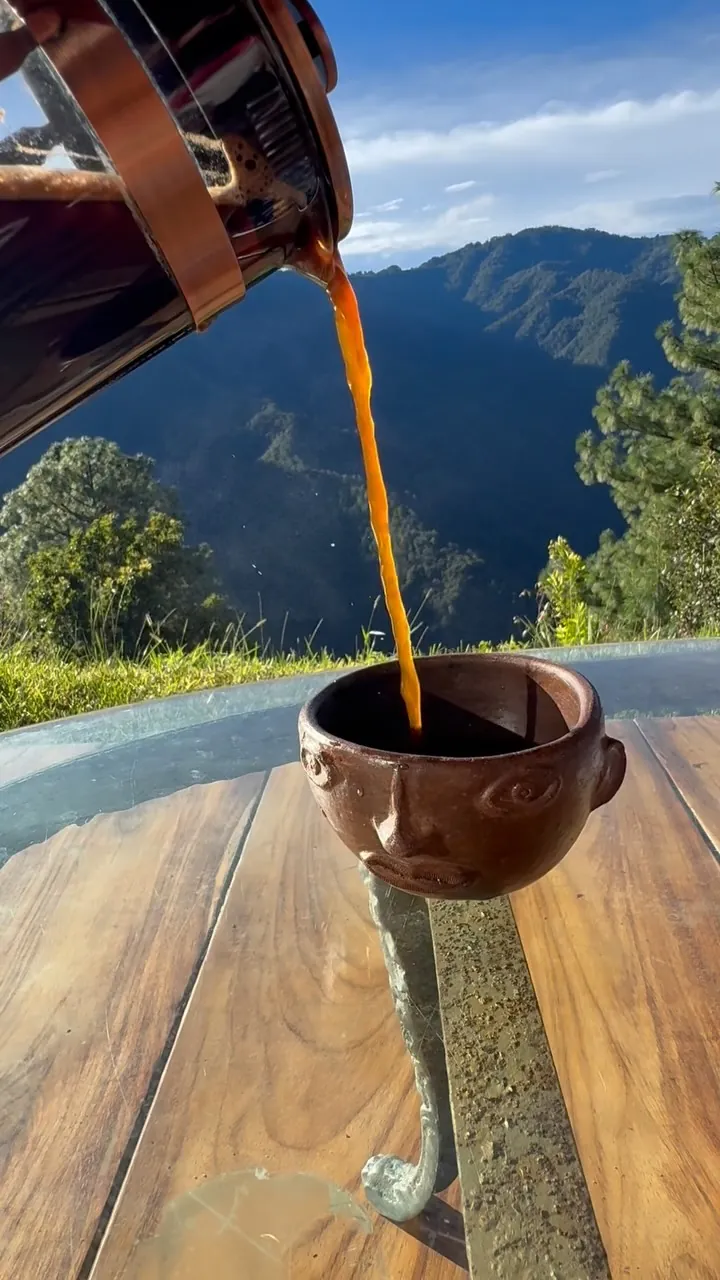 Café recién hecho servido en una taza de barro sobre la mesa, la sierra al fondo.