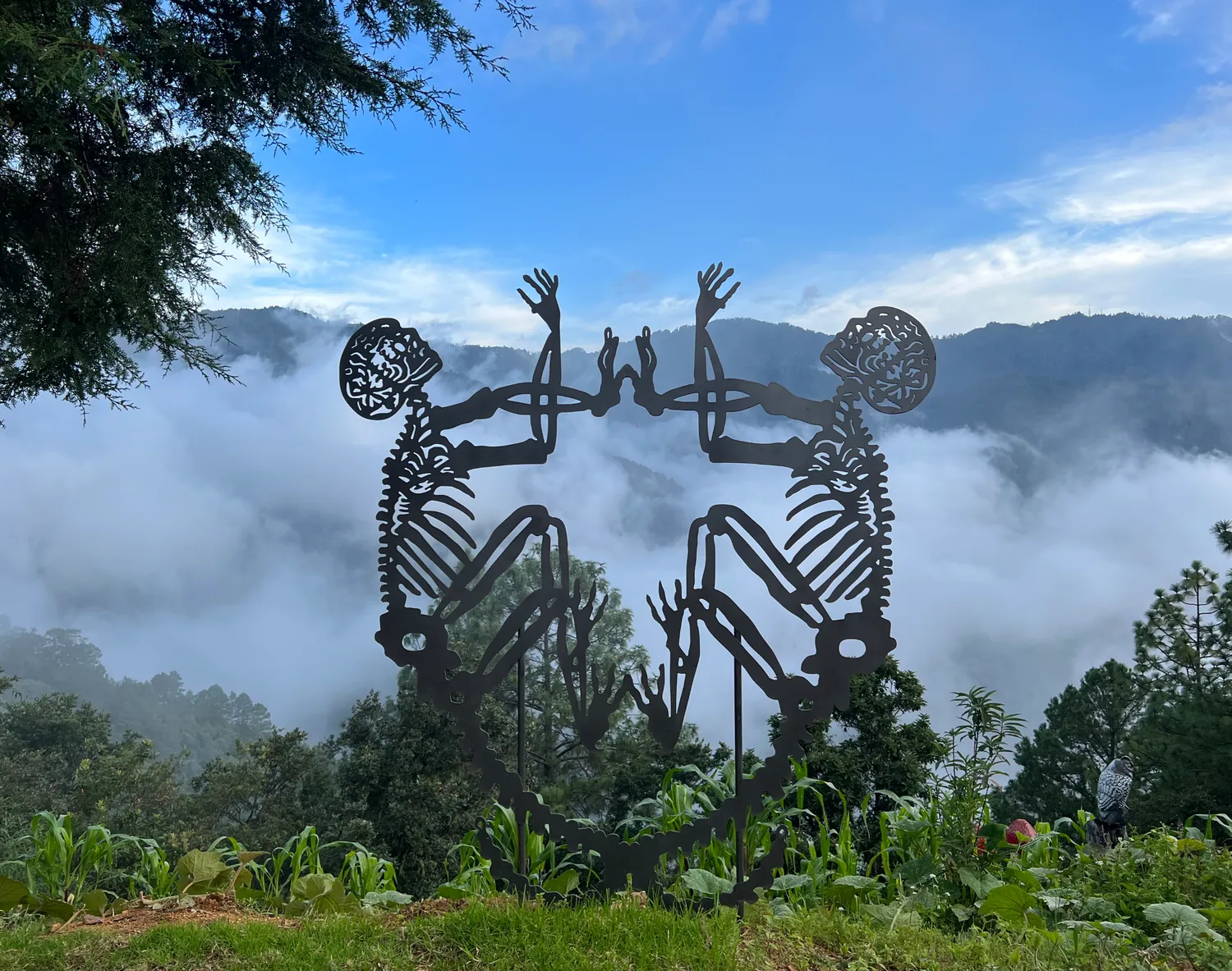 Escultura de metal de dos figuras sentadas frente a las nubes del valle.