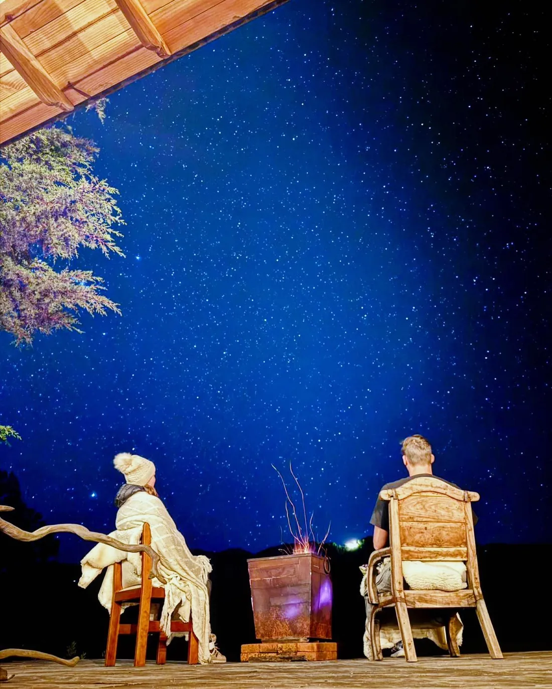 Dos personas junto a un brasero en la terraza bajo un cielo estrellado.